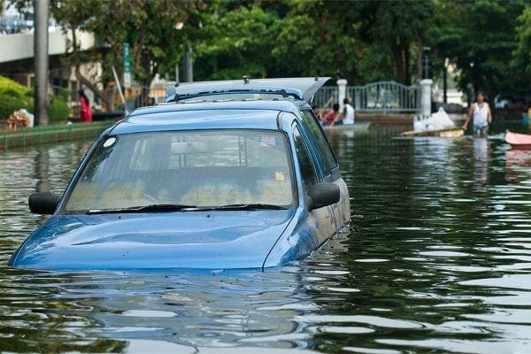 Blue car submerged in floodwater on a city street.